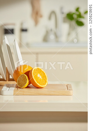 Beige kitchen table top for product presentation, was shot from front view over blurred contemporary kitchen interior background. Fresh oranges featured on wooden cutting board, copy space for text 120828691