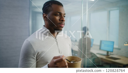 African American office worker eats food taking break during lunch in modern office 120828764