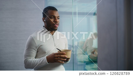 African American businessman eats food, chats with business partner using headphones 120828789