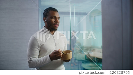 African American businessman eats food, chats with business partner using headphones African American businessman eats food, chats with business partner using headphones 120828795
