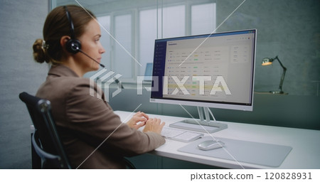 Female marketing specialist talks on headset with client, works on computer 120828931