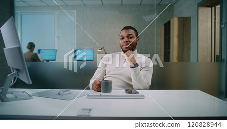 Portrait of African American businessman sitting at the workplace, smiling and looking at camera 120828944