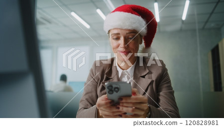Female marketing specialist in Santa hat chats with business partner using mobile phone 120828981