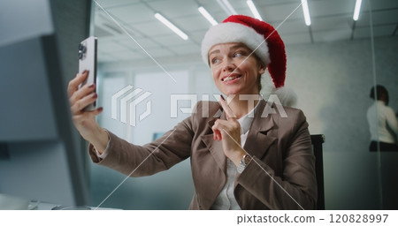 Businesswoman in Christmas hat talks to business partner on video call using smartphone Businesswoman in Christmas hat talks to business partner on video call using smartphone 120828997