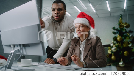 Female marketing specialist in Christmas hat uses computer with African American colleague Female marketing specialist in Christmas hat uses computer with African American colleague 120829003