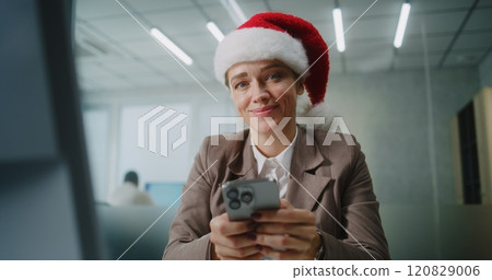 Female marketing specialist in Santa hat chats with business partner using mobile phone Female marketing specialist in Santa hat chats with business partner using mobile phone 120829006