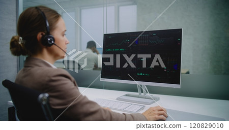 Female stockbroker talks on headset, analyzes financial charts and diagrams on computer 120829010