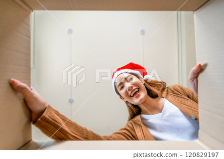 Low angle view of surprised young Asian woman wearing Christmas hat and unpacking 120829197