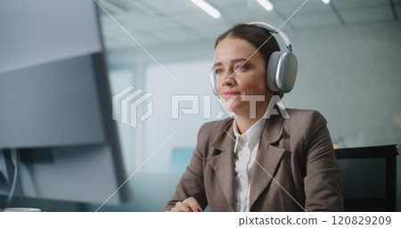 Businesswoman wearing headphones works on computer, chats with business partner Businesswoman wearing headphones works on computer, chats with business partner 120829209