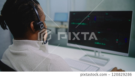 African American financial specialist in headset analyzes share market and stocks on computer 120829286