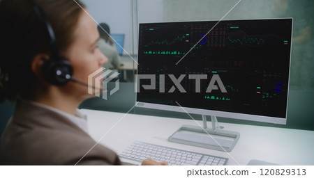Female financial specialist talks on headset with investor, analyzes share market and stocks on computer Female financial specialist talks on headset with investor, analyzes share market and stocks on computer 120829313