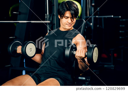 Asian man Muscular guy lifting dumbbell while sitting on bench gym, men using dumbbell during workout pumping up bicep muscle at fitness gym, workout healthy lifestyle concept 120829699