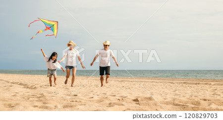 Asian family is flying a kite high in the sky while running on the beach. Happy parents mother and father with their child playing with kite, family is enjoying their time together, summer day Asian family is flying a kite high in the sky while running on the beach. Happy parents mother and father with their child playing with kite, family is enjoying their time together, summer day 120829703