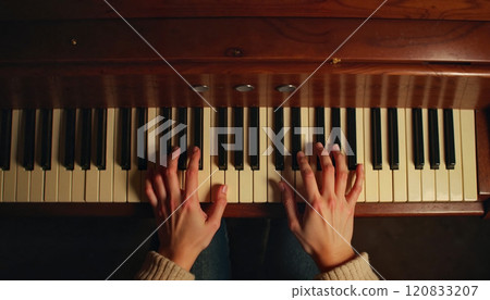 Playing melodies on an old wooden piano surrounded by soft ambient light during a cozy evening at home Playing melodies on an old wooden piano surrounded by soft ambient light during a cozy evening at home 120833207