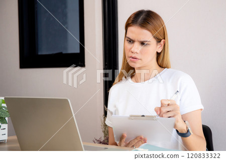 Portrait young businesswoman using laptop computer while writing on note on desk in living room. Portrait young businesswoman using laptop computer while writing on note on desk in living room. 120833322