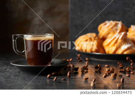 Black coffee in glass cup and coffee beans in motion on a black table. Black coffee in glass cup and coffee beans in motion on a black table. 120834473