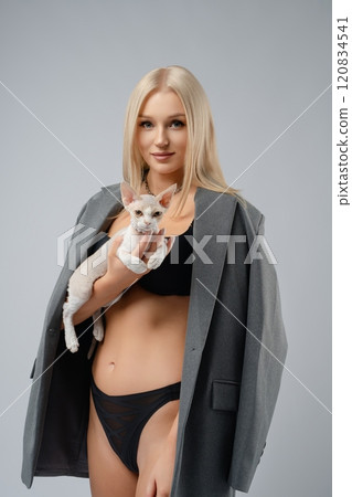 Young woman holds a cat while wearing a stylish oversized blazer indoors Young woman holds a cat while wearing a stylish oversized blazer indoors 120834541