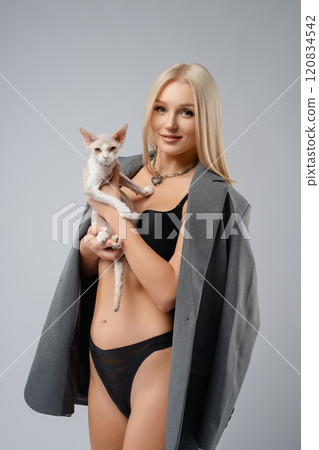 Young woman poses confidently with a cat in a stylish studio setting 120834542