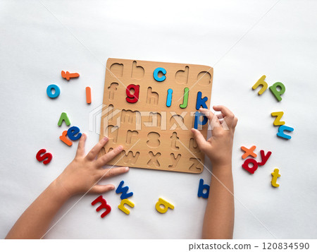 Childs hands solving colorful alphabet puzzle for learning and play 120834590