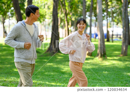 Cheerful asian woman and her father jogging through a scenic park in the morning Cheerful asian woman and her father jogging through a scenic park in the morning 120834634
