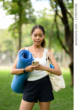 Beautiful young African woman checking her smartphone After yoga session in a park 120834706