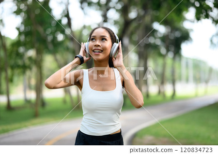 Young woman wearing sporty outfit enjoying music with headphones in a park 120834723