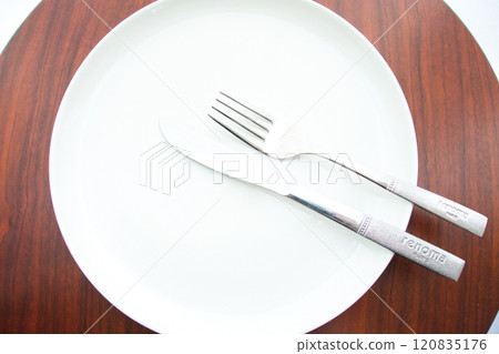 Wait for the next dish by green dish and cutlery placed on a brown table Wait for the next dish by green dish and cutlery placed on a brown table 120835176