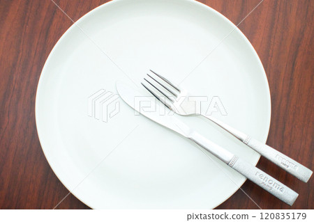 Wait for the next dish by green dish and cutlery placed on a brown table Wait for the next dish by green dish and cutlery placed on a brown table 120835179