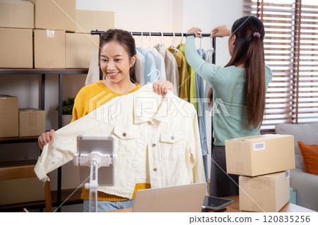 Two young asian woman live online clothing store while showing clothing with tablet and laptop. Two young asian woman live online clothing store while showing clothing with tablet and laptop. 120835256