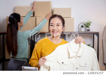 Two young asian woman live online clothing store while showing clothing with tablet on social. 120835257