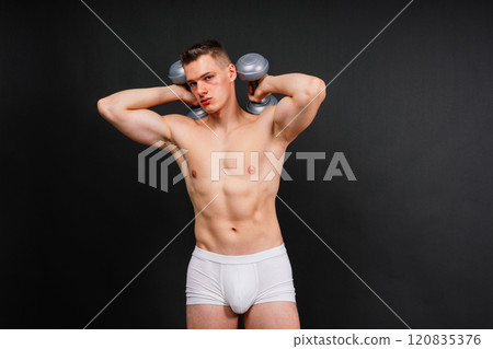 Muscular young man in white underwear with dumbbell in studio background Muscular young man in white underwear with dumbbell in studio background 120835376