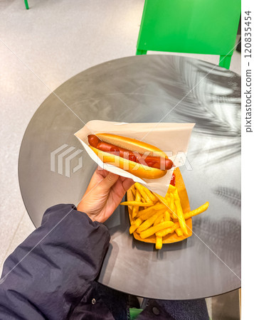 female Hand holding a hot dog with fries on a plate on wooden table . High quality photo female Hand holding a hot dog with fries on a plate on wooden table . High quality photo 120835454