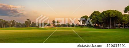 A tranquil golf course bathed in warm evening light, surrounded by lush trees and open greens, offering a serene outdoor escape. 120835691