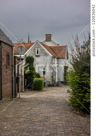 A peaceful alley with cobblestone paving, surrounded by charming houses with red-tiled roofs and lush greenery. A bike rests near a white house, creating a tranquil, village-like atmosphere. A peaceful alley with cobblestone paving, surrounded by charming houses with red-tiled roofs and lush greenery. A bike rests near a white house, creating a tranquil, village-like atmosphere. 120836042
