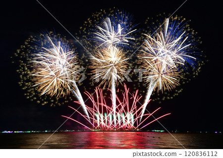 Multi-colored fireworks are launched in the middle of the sea from a large steel ship . 120836112