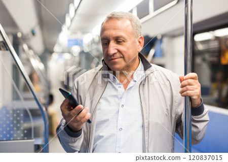 Positive elderly passenger communicates on mobile phone in subway car 120837015