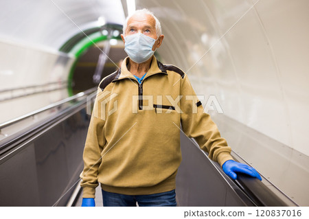 Elderly man in protective mask moving up on escalator while leaving subway station platform 120837016
