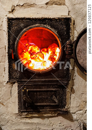 Close-up of burning wood logs inside a furnace with bright flames and glowing embers. 120837125