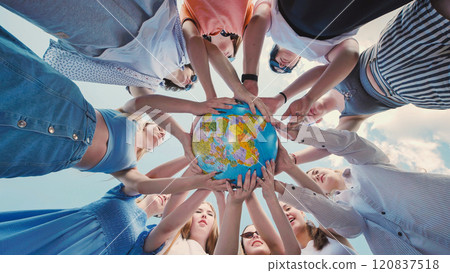 Group of young people is standing in a circle, holding a globe in their hands against a blue sky. Group of young people is standing in a circle, holding a globe in their hands against a blue sky. 120837518
