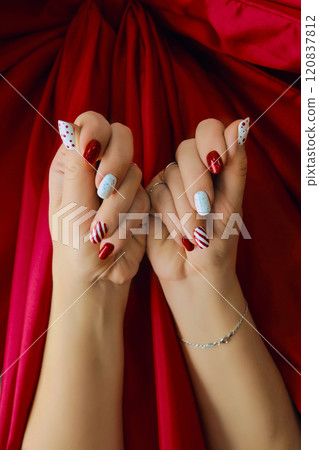 Woman's hand with oval red Nails with a design in the style of classic Christmas balls and candy Woman's hand with oval red Nails with a design in the style of classic Christmas balls and candy 120837812