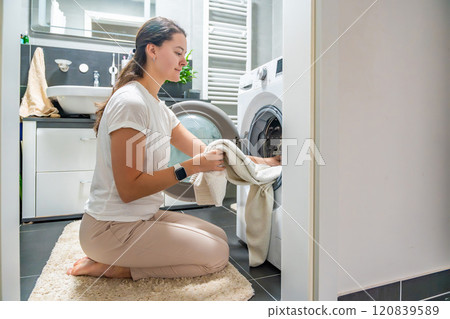 Young woman Inserting clothes inside the washing machine In home bathroom Young woman Inserting clothes inside the washing machine In home bathroom 120839589