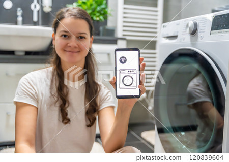 Young woman using mobile phone control via wi-fi and app for washing machine in home. Homesmart and new technology concept Young woman using mobile phone control via wi-fi and app for washing machine in home. Homesmart and new technology concept 120839604