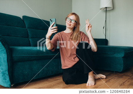 Hi. Female in taking a selfie photo using her mobile phone at home. People lounge concept. 30s girl showing peace sign with fingers. Full Body 120840284