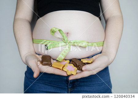 Obesity and overweight from overeating. Big belly tied with measuring tape as a gift. Body fat from candies and sweets Obesity and overweight from overeating. Big belly tied with measuring tape as a gift. Body fat from candies and sweets 120840334