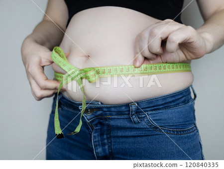 Obesity and overweight from overeating. Big belly tied with measuring tape as a gift. Body fat from candies and sweets 120840335