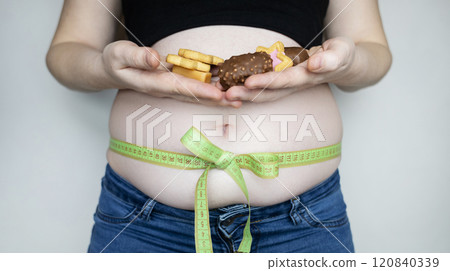 Obesity and overweight from overeating. Big belly tied with measuring tape as a gift. Body fat from candies and sweets 120840339