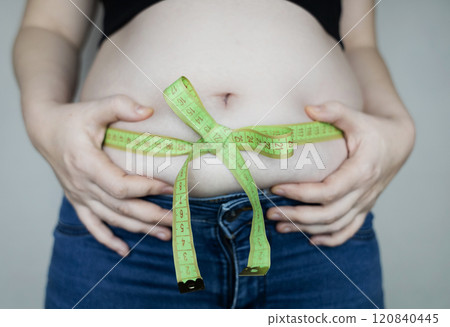 Obesity and overweight from overeating. Big belly tied with measuring tape as a gift. Body fat from candies and sweets Obesity and overweight from overeating. Big belly tied with measuring tape as a gift. Body fat from candies and sweets 120840445