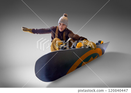 Man in winter gear balances on his snowboard, showcasing dynamic movement and control, against gray studio backdrop. 120840447