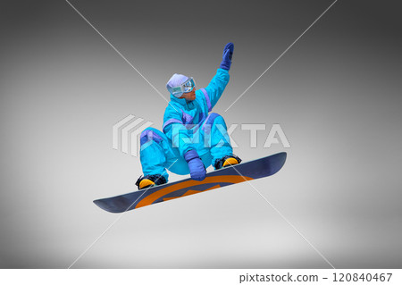 Dynamic photo of young athletic man in retro blue jumping suit performing in mid air in motion dramatic trick against grey studio background. Dynamic photo of young athletic man in retro blue jumping suit performing in mid air in motion dramatic trick against grey studio background. 120840467
