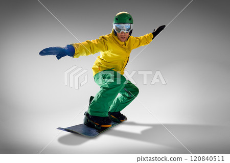 Young athletic man dressed modern, bright yellow and green suit slopes in action against grey studio background. Low angle. 120840511